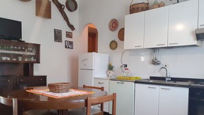 Una cocina compacta con armarios blancos, una mesa de comedor con sillas y un refrigerador.
