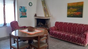 Una sala de estar con una mesa redonda de madera, un sofá rojo estampado, una chimenea y arte en la pared.