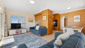 Uma sala de estar moderna com sofá, TV e área de jantar com mesa e cadeiras.