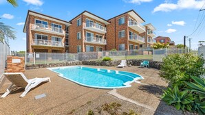 Um edifício residencial com piscina, várias varandas e um quintal cercado.