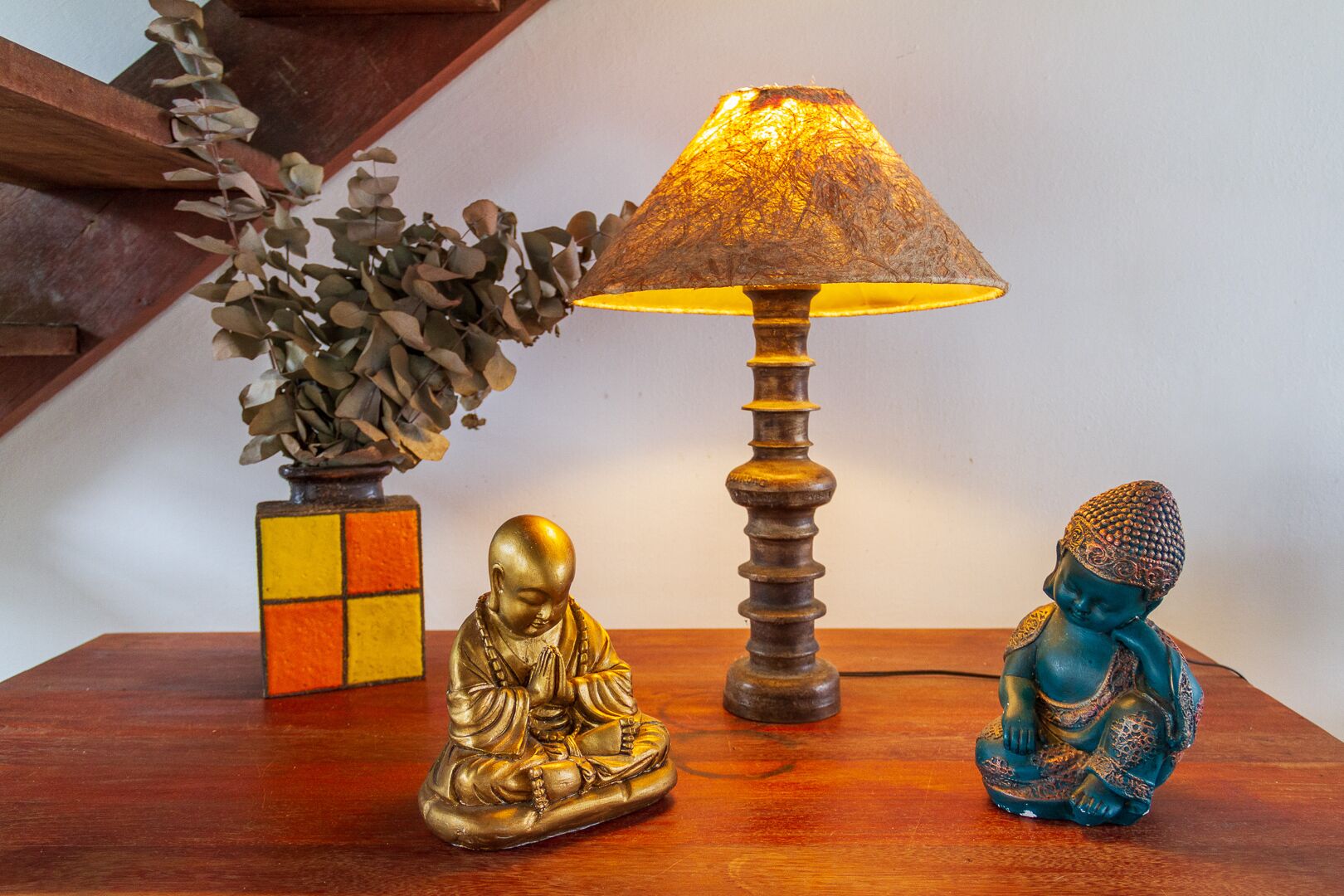 Een houten tafel met een Boeddhabeeld, een lamp en een plant in een pot.