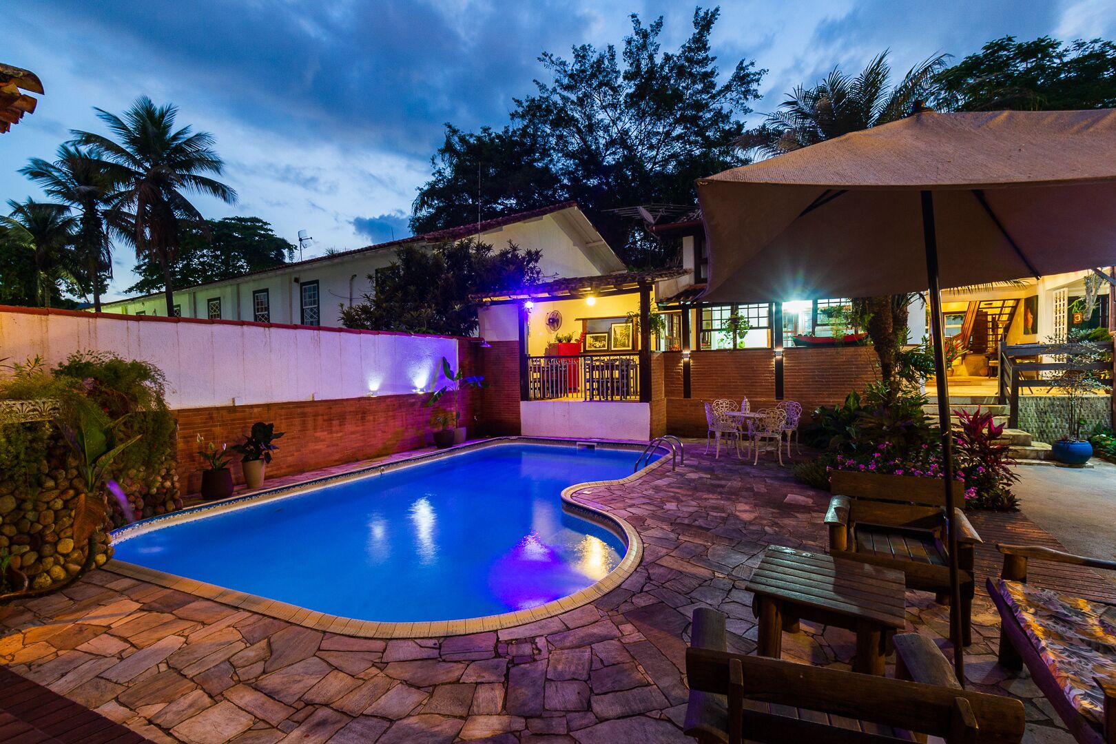 A swimming pool with a stone deck, surrounded by a patio area with outdoor seating and a covered section.