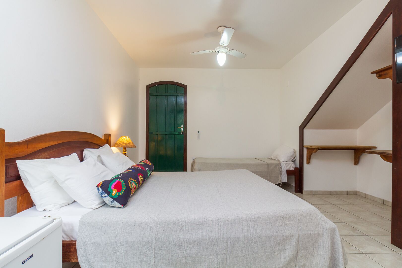 A bedroom with a bed, a bedside table, a lamp, a wardrobe, and a ceiling fan.