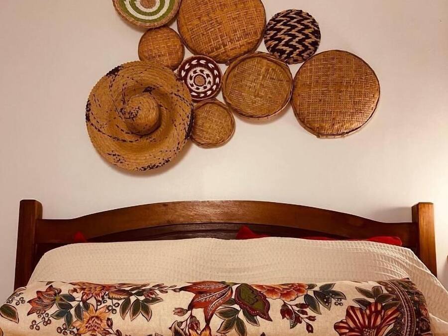 Una cama con un cojín estampado con flores y una pared decorada con cestas tejidas.