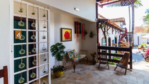 Un patio con suelo de piedra, un banco de madera, una silla, una mesa, una planta en maceta y una exhibición de terrarios de vidrio montada en la pared.
