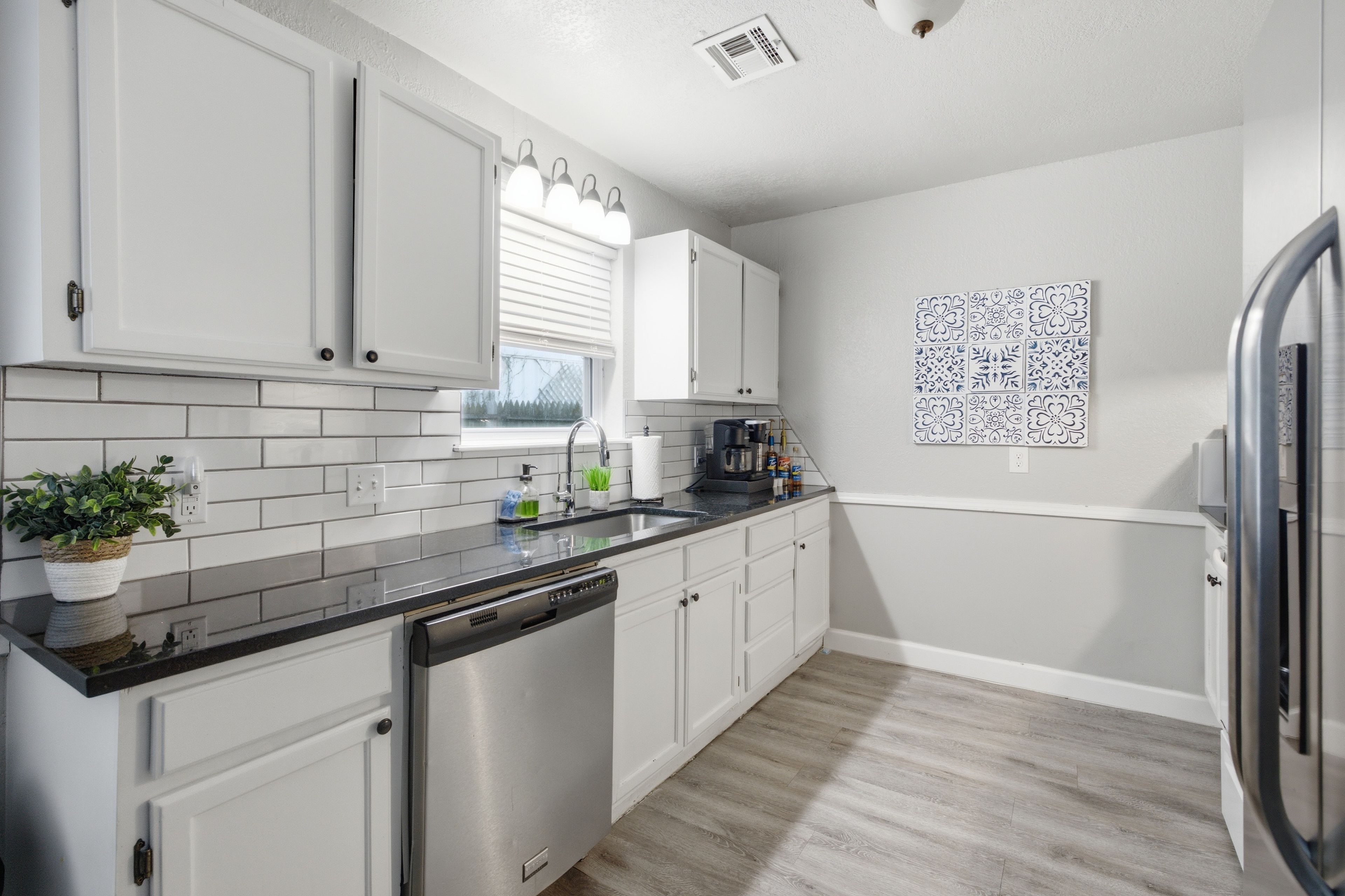 A modern kitchen with white cabinetry, a dishwasher, and a stainless steel refrigerator.