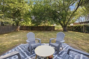 An outdoor seating area with two Adirondack chairs and a small round table, surrounded by a patterned outdoor rug. - Cozy 3BR family retreat with a fenced backyard, patio, and everything you need for a comfortable stay in Broken Arrow. Pet friendly! (Broken Arrow)