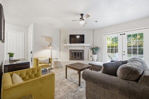 A living room with a fireplace, a ceiling fan, and a large window.