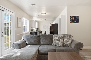 A modern living room with a sectional sofa, a dining table, and a kitchen in the background.