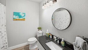 Een badkamer met toilet, wastafel, spiegel en een schilderij aan de muur.