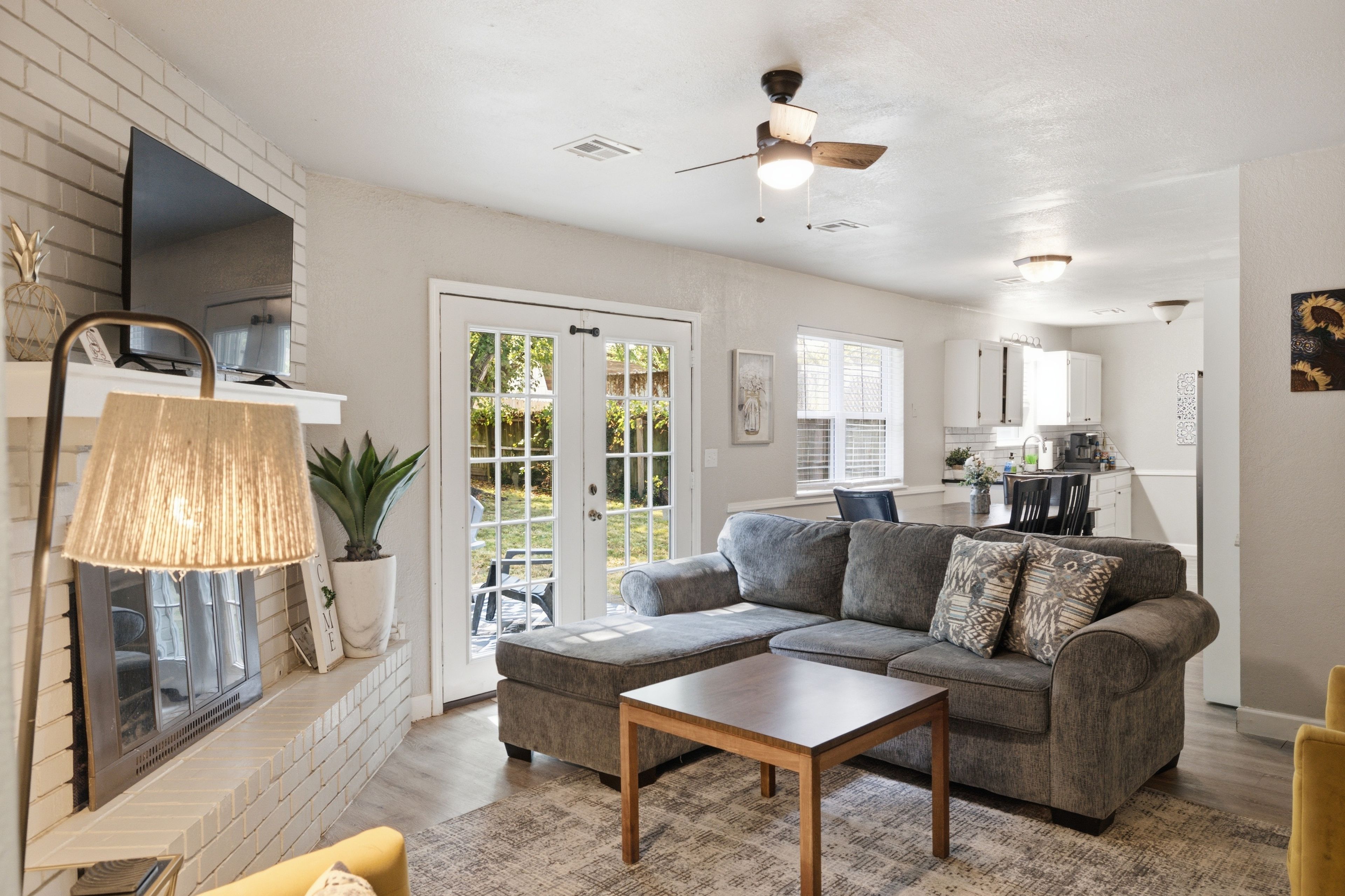 A spacious living room with a grey sectional sofa, a coffee table, and a TV mounted on the wall.