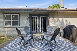 Eine Terrasse mit Tisch, vier Stühlen, einem Grill und einem Haus mit Schornstein.