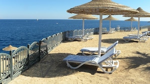 A beach with sun loungers and thatched umbrellas, a metal railing, and the sea in the background. - Grand Halomy resort (Sharm El Sheikh)