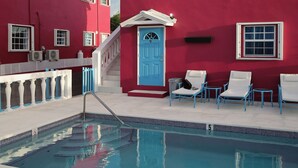 A red building with a pool, blue chairs, and a blue door. - Forget your worries in this serene space. Pool view, top floor. Privacy gate. (Blue Hills)