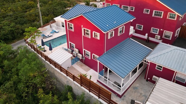 A large, red, two-story house with a blue roof, a swimming pool, and a fenced patio area. - Forget your worries in this serene space. Pool view, top floor. Privacy gate. (Blue Hills)