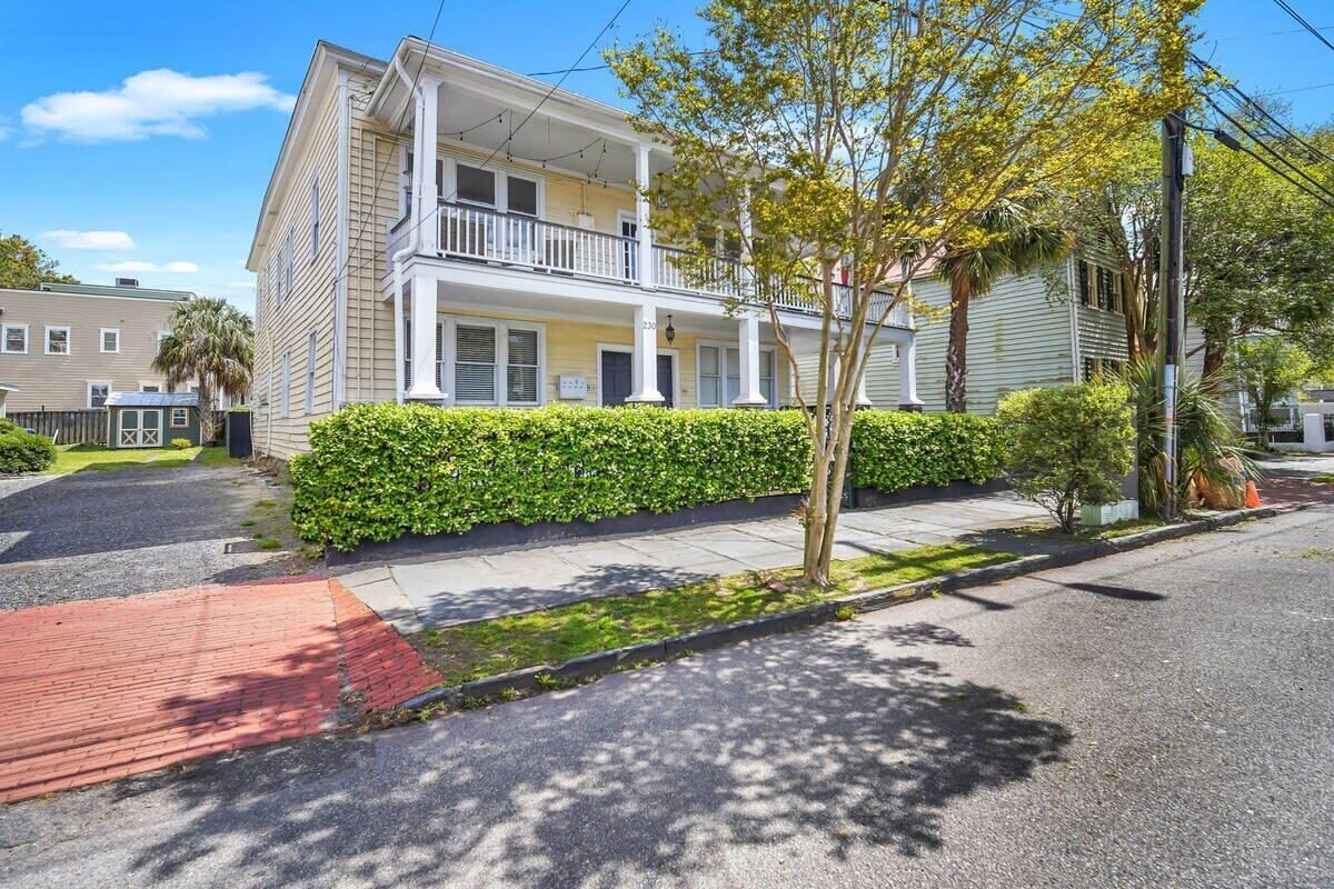 A two-story building with a balcony on the second floor, a covered front porch, and a well-maintained hedge along the sidewalk.