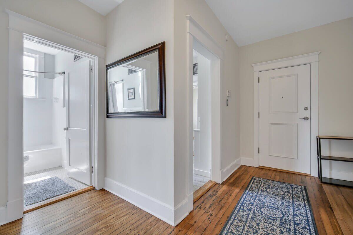A hallway with wooden flooring, white walls, and a blue patterned rug. There are white doors leading to a bathroom and a closet.