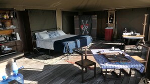 Ein kleiner, übersichtlicher Raum mit Bett, Tisch, Stuhl und einem Regal mit diversen Gegenständen.