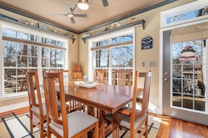 A dining area with a wooden table and chairs, large windows, and a 'Welcome' sign.