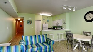 A compact living space with a sofa, dining table, chairs, a kitchen area, and a hallway. - Shores of Panama 524 | Pool, Spa, Gym! (Panama City Beach)