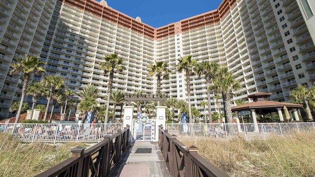 A high-rise hotel with multiple balconies, palm trees, and a gated entrance. - Shores of Panama 524 | Pool, Spa, Gym! (Panama City Beach)