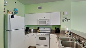 A compact kitchen with white cabinets, a microwave, a stove, and a refrigerator. - Shores of Panama 524 | Pool, Spa, Gym! (Panama City Beach)