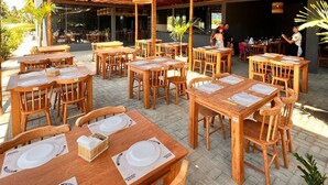 An outdoor dining area with wooden tables and chairs, thatched roof, and hanging wicker lamps. - Flat I 002 Villas Manatee Patacho - AL (Porto de Pedras)