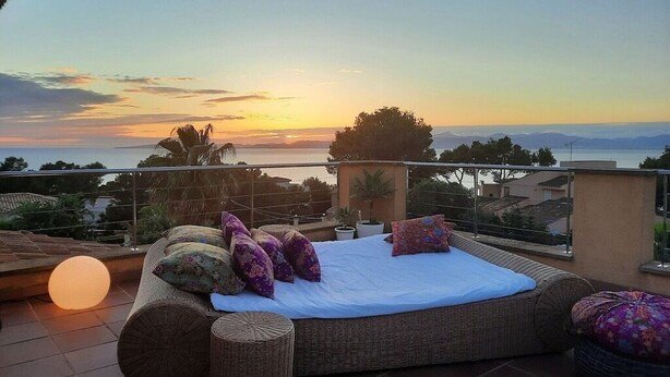 A balcony with a wicker sofa, pillows, and a view of the sunset over the sea. - Design Villa Bahia Azul, roof terrace with panoramic sea view, nice garden, pool (Badia Blava)