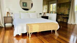 A modern bedroom with a large bed, a round mirror, a bedside table, and a wicker bench. - Design Villa Bahia Azul, roof terrace with panoramic sea view, nice garden, pool (Badia Blava)