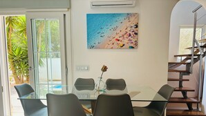 A modern dining area with a glass table, black chairs, and a beach-themed painting on the wall. - Design Villa Bahia Azul, roof terrace with panoramic sea view, nice garden, pool (Badia Blava)