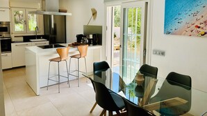 A modern kitchen with white cabinets, stainless steel appliances, and a glass dining table with black chairs. - Design Villa Bahia Azul, roof terrace with panoramic sea view, nice garden, pool (Badia Blava)