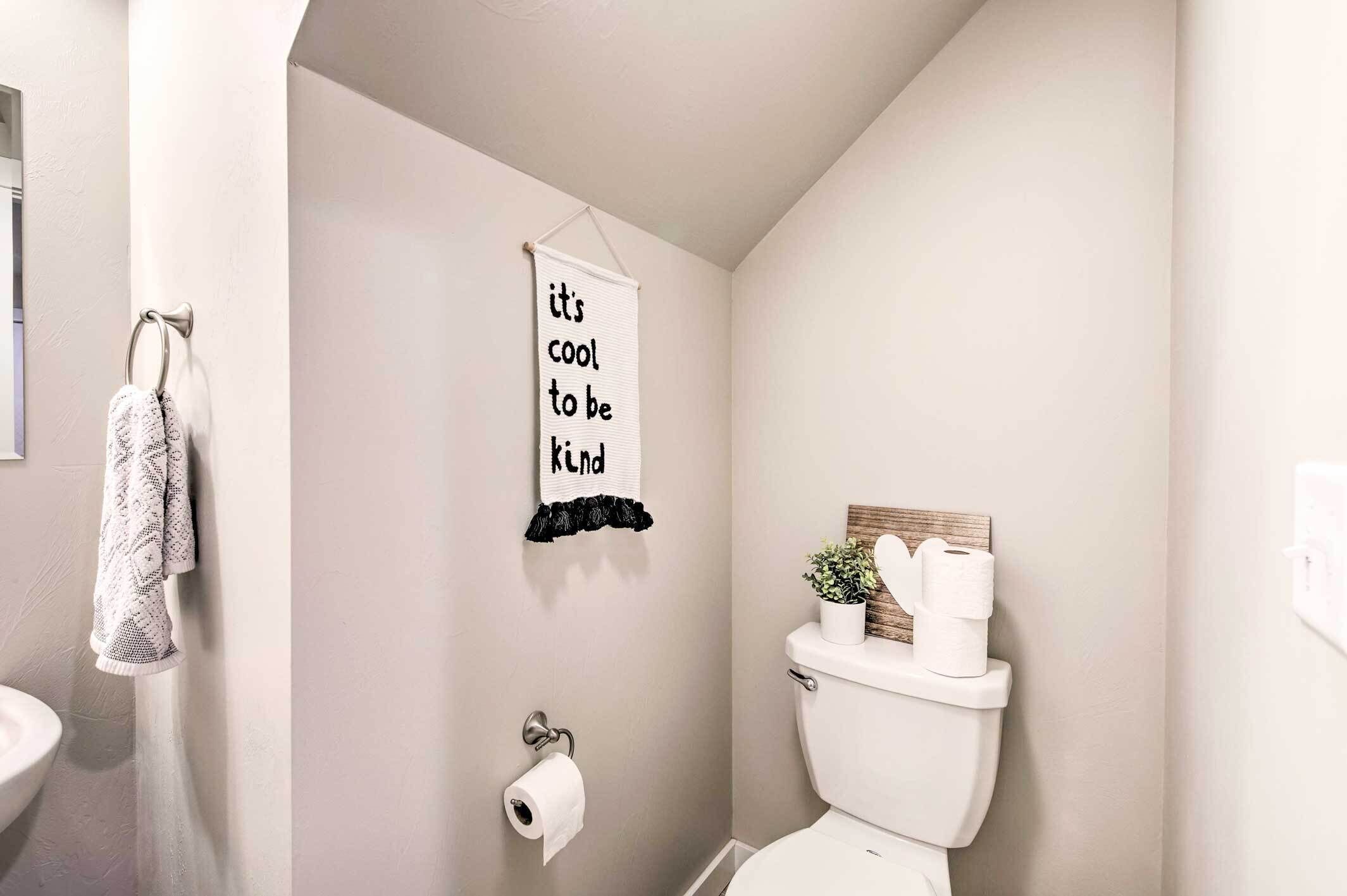 Un baño con inodoro, un perchero con toalla estampada, dispensador de papel higiénico y un cartel en la pared.