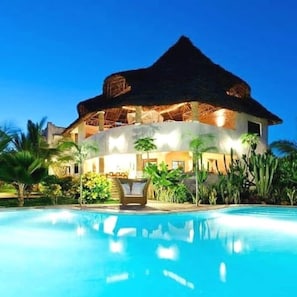 Une grande maison avec une piscine, entourée de plantes tropicales.