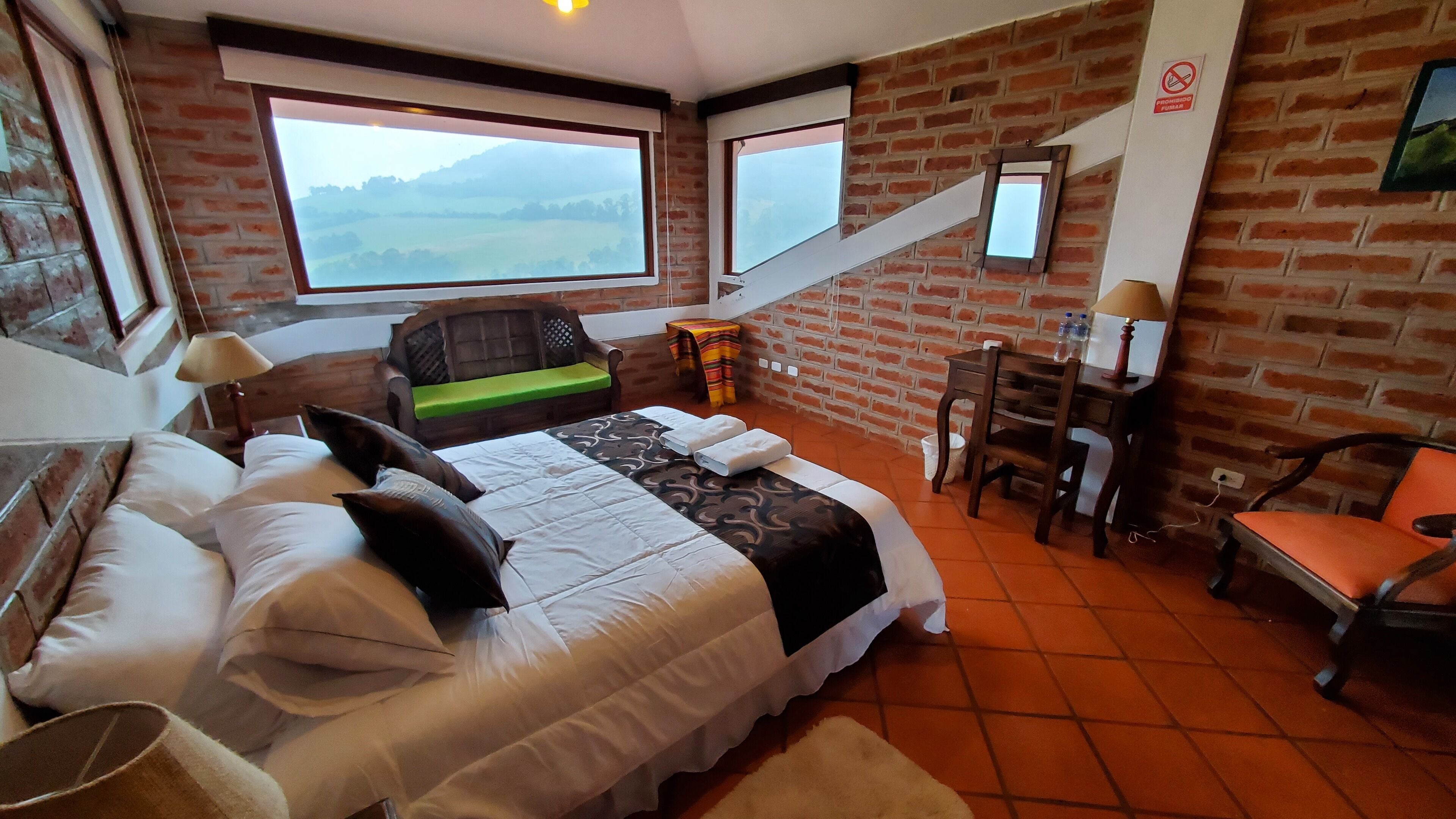 Un dormitorio con cama, escritorio, silla, mesita y ventana con vista al paisaje.