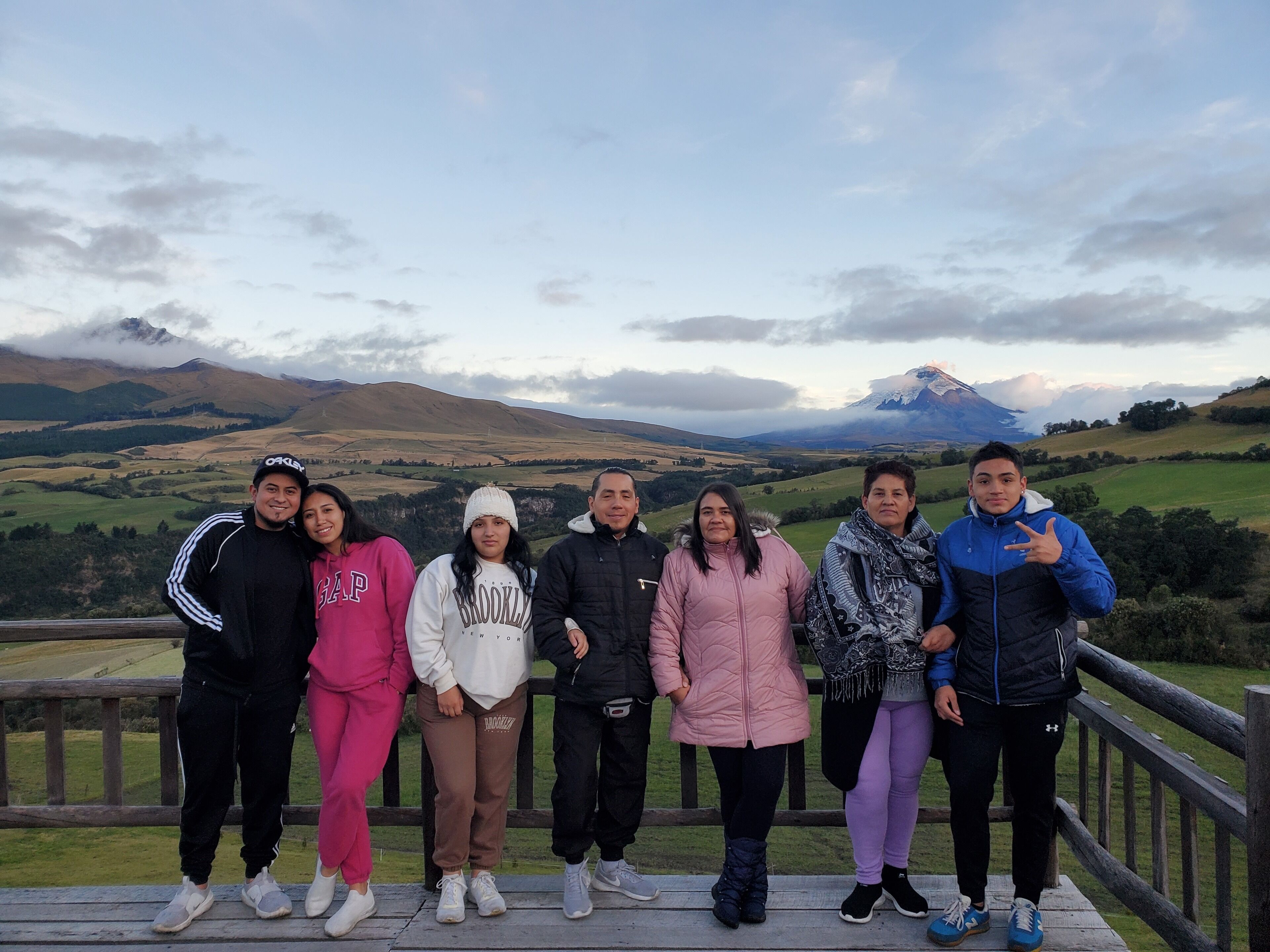A group of people standing on a wooden deck with a scenic mountain view in the background.