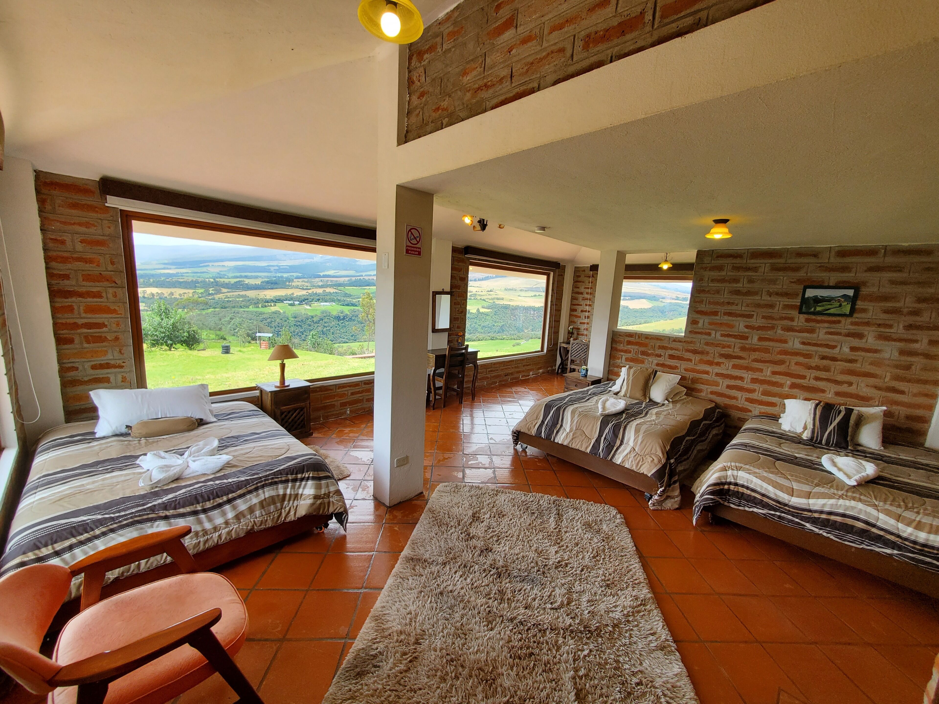 Un dormitorio amplio con dos camas, un ventanal grande que ofrece vistas panorámicas y una pared de ladrillo rústica.