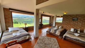 Un dormitorio amplio con dos camas, un ventanal grande que ofrece vistas panorámicas y una pared de ladrillo rústica.