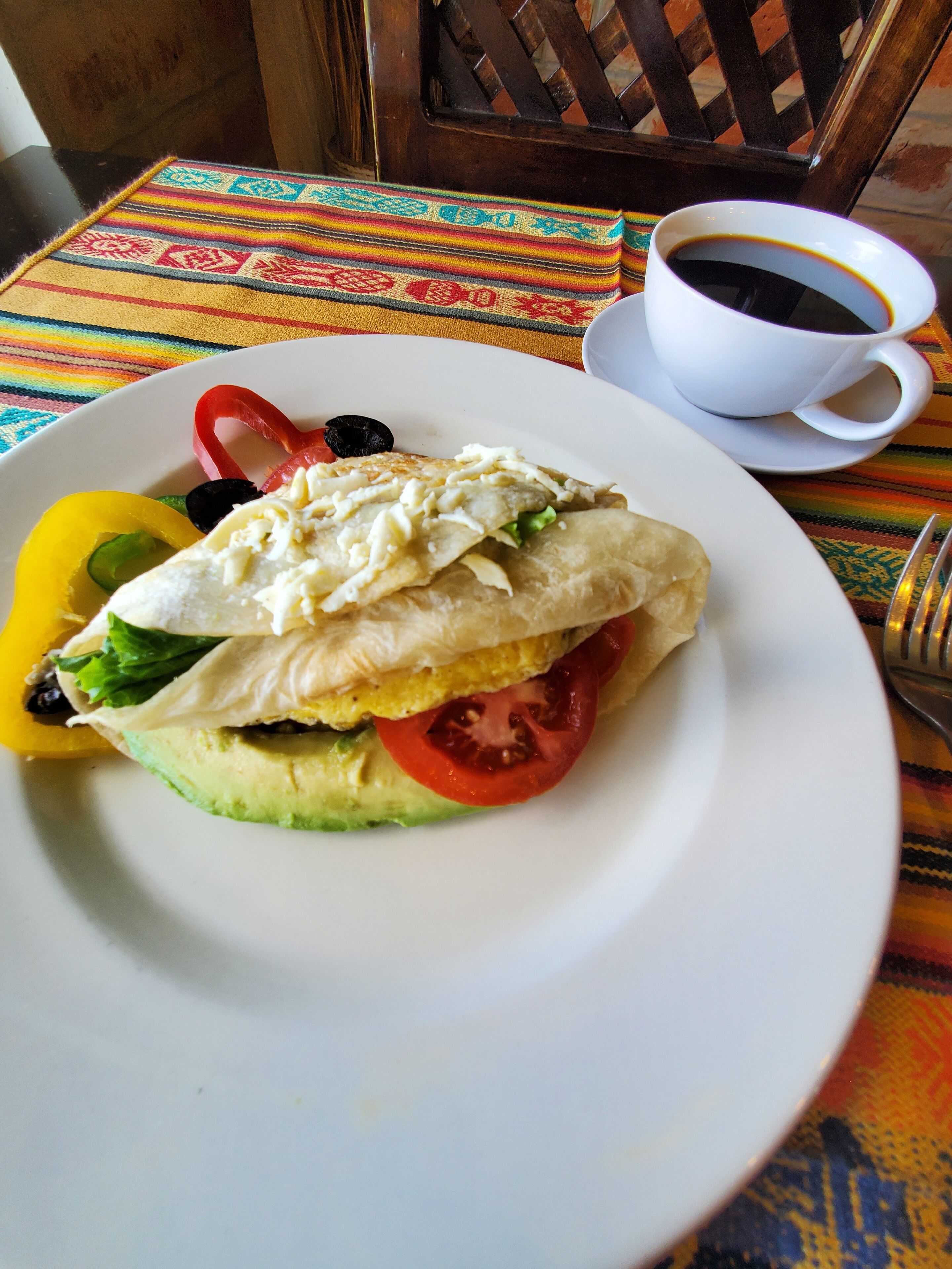 A plate with a sandwich, a cup of coffee, and a colorful tablecloth.