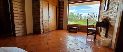 A room with a large window, a wooden wardrobe, and a tiled floor.