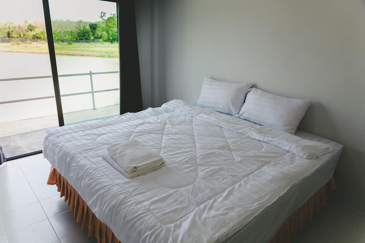 Un lit bien fait, avec une couette blanche et des oreillers, une serviette pliée, et une vue sur un paysage verdoyant par une porte vitrée.