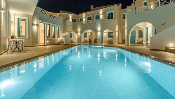 A swimming pool with a clear blue water surface, surrounded by a building with multiple balconies and arched doorways. - Nikolas Hotel (Santorini)