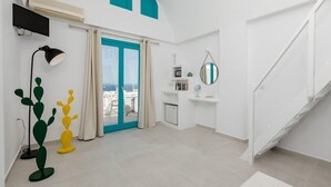 A modern living room with a sliding glass door leading to a balcony, a small desk with a mirror, and a staircase. - Nikolas Hotel (Santorini)
