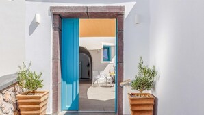 A narrow entrance with a blue door leading to a patio area with outdoor furniture. - Nikolas Hotel (Santorini)