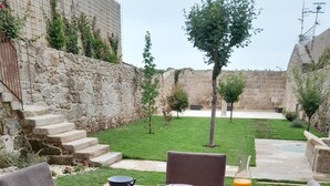 An outdoor dining area with stone walls, a grassy lawn, and a view of ancient ruins. - Acouga Hotel Boutique (Celanova)