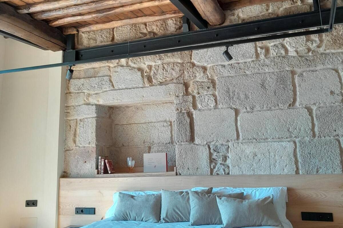 A bedroom with a stone wall headboard, a wooden ceiling, and a bed with pillows.
