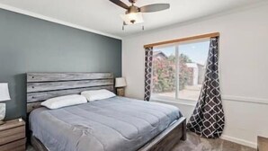 Een slaapkamer met een bed, een plafondventilator, een raam met gordijnen en een nachtkastje met een lamp.