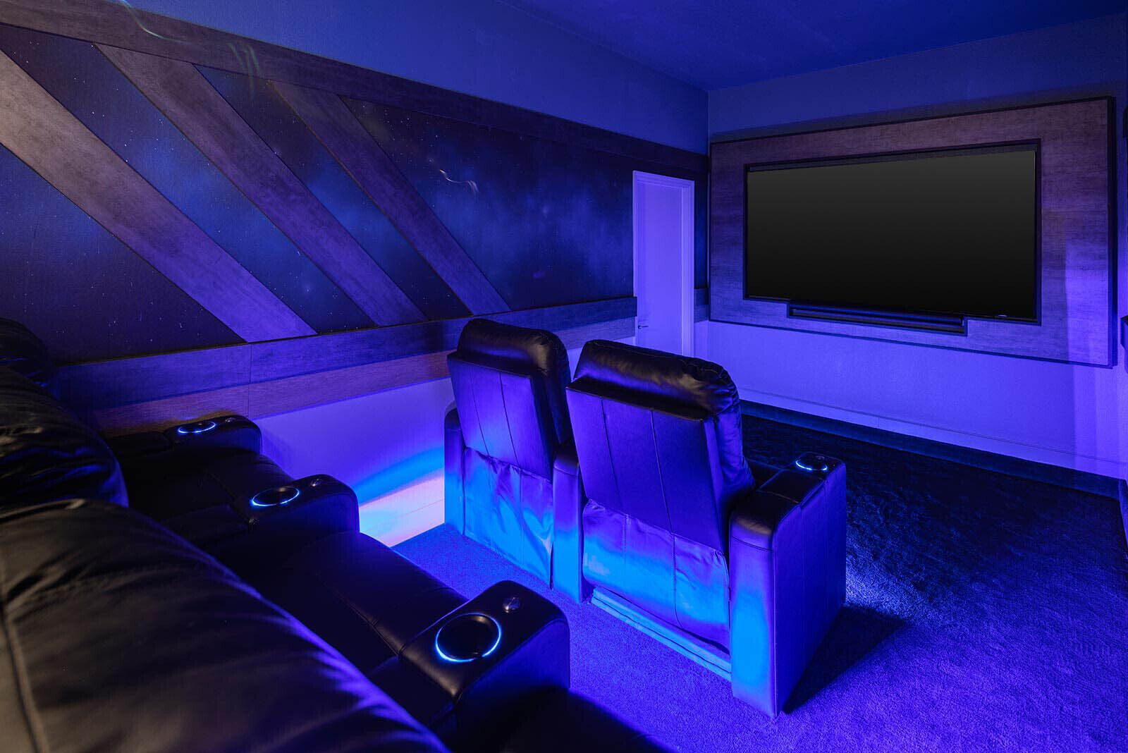 A home theater room with a large screen, two reclining chairs, and a wooden ceiling.