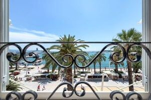 A balcony with a view of a beachside promenade, palm trees, and the sea.