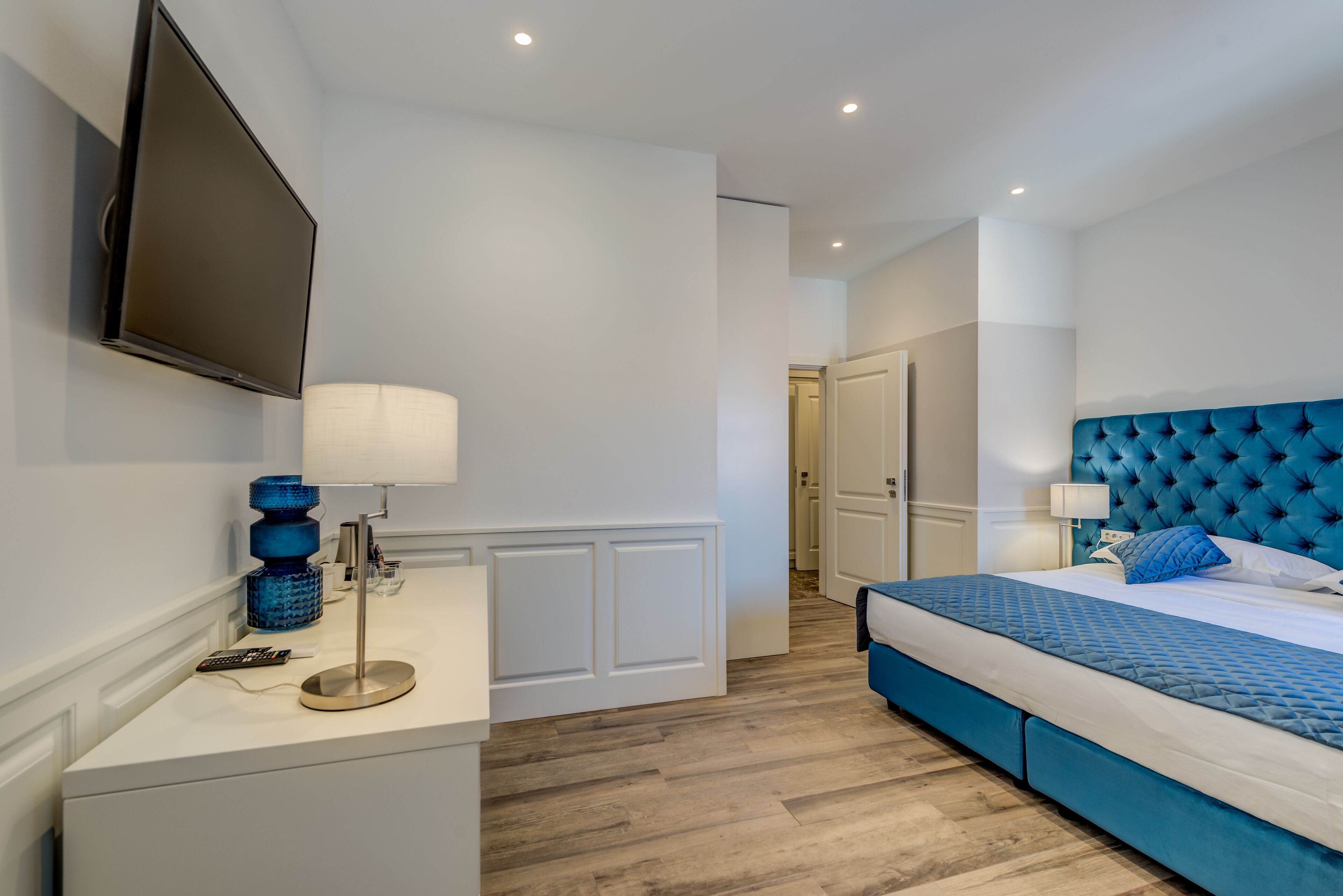 Une chambre à coucher moderne avec un grand lit, un téléviseur fixé au mur et une table de chevet avec une lampe.