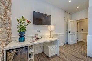 A modern hotel room with a white console table, a mounted flat-screen TV, a coffee maker, and a vase with flowers.